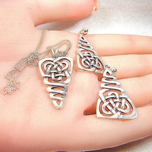 May include: A silver Celtic knot pendant necklace and matching earrings. The pendant and earrings feature intricate knotwork designs. The necklace has a delicate chain. The earrings are dangling style. The jewellery is displayed on a light background.