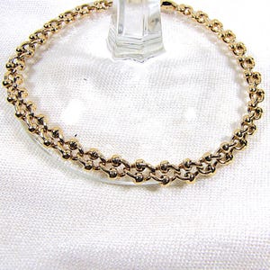 May include: A gold-colored bracelet with a double-strand chain design. The bracelet features small, round beads connected by delicate links, creating a textured and elegant appearance. The jewelry is displayed on a clear glass surface.