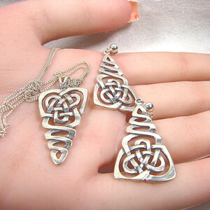 May include: A silver pendant necklace and matching earrings set. The pendant and earrings feature a Celtic knot design with a spiral base. The jewellery is displayed on a light background.