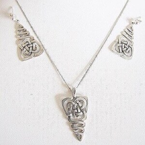 May include: A silver-coloured jewellery set with a Celtic knot design. The set includes a pendant necklace and matching earrings. The pendant and earrings have a detailed, openwork design, and the necklace has a delicate chain.