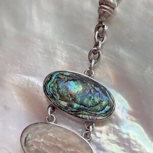 May include: A silver chain with a clasp and two oval-shaped abalone shell charms. The charms are iridescent with shades of green, blue, and purple.