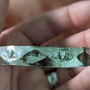 May include: Silver bangle bracelet with a diamond-shaped design and a hallmark of "925" on the inside.