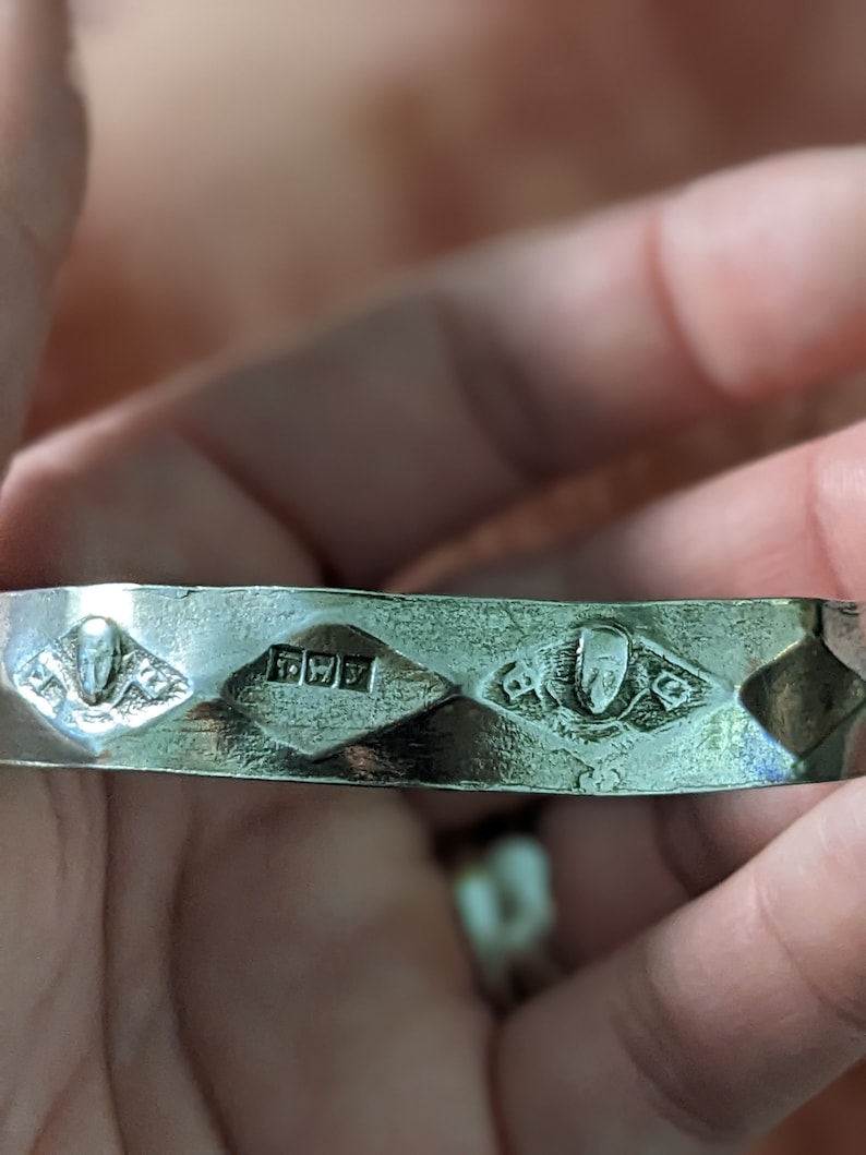 May include: Silver bangle bracelet with a diamond-shaped design and a hallmark of "925" on the inside.