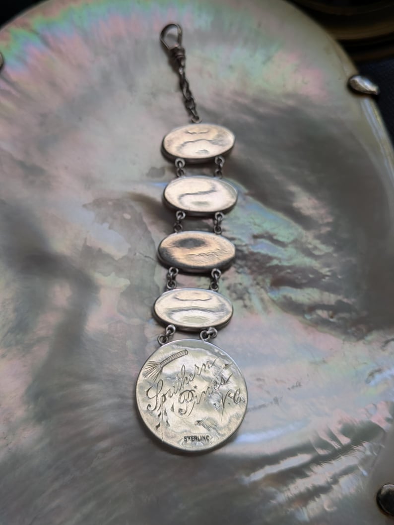 May include: A silver charm bracelet with five oval charms. The bottom charm is engraved with the text "Southern Princess Vela" and "Sterling".