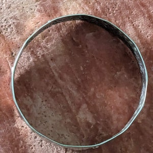 May include: A silver metal bangle bracelet with a textured surface.