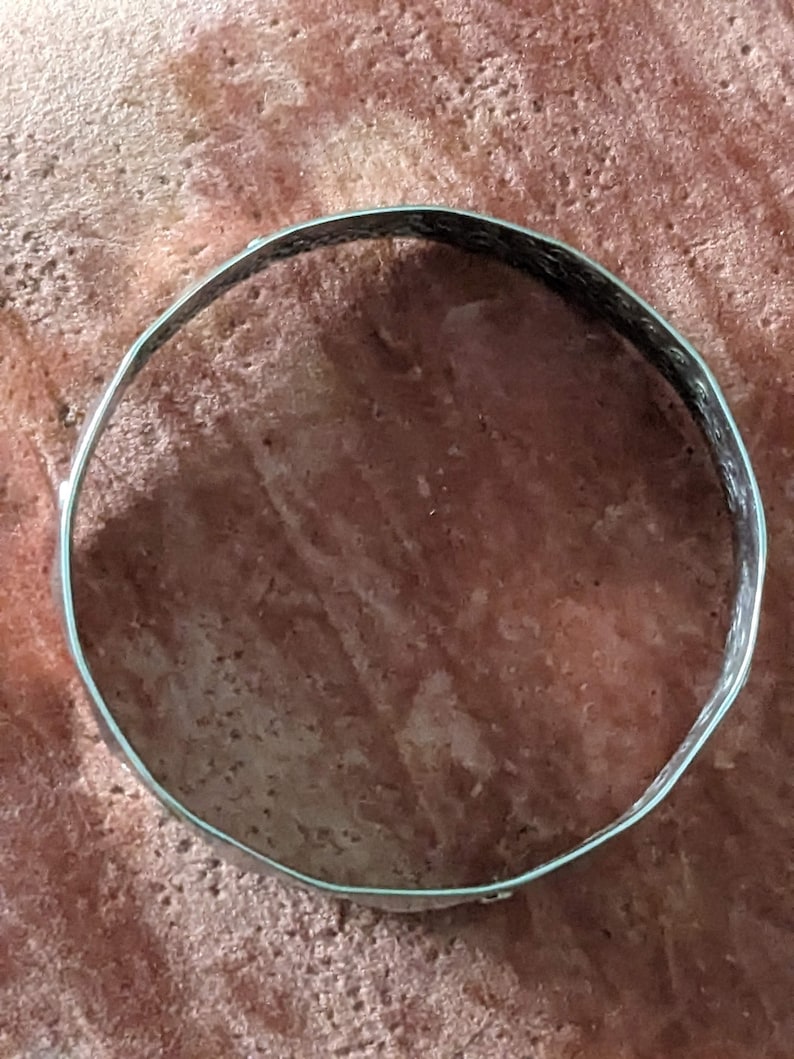 May include: A silver metal bangle bracelet with a textured surface.