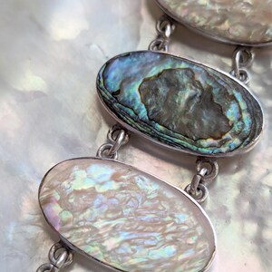 May include: A silver bracelet with oval-shaped abalone shell charms. The shells have iridescent colors of blue, green, and purple.