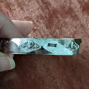 May include: A silver bracelet with a textured design and three diamond-shaped markings. The markings include the letters "925" and "FWY".