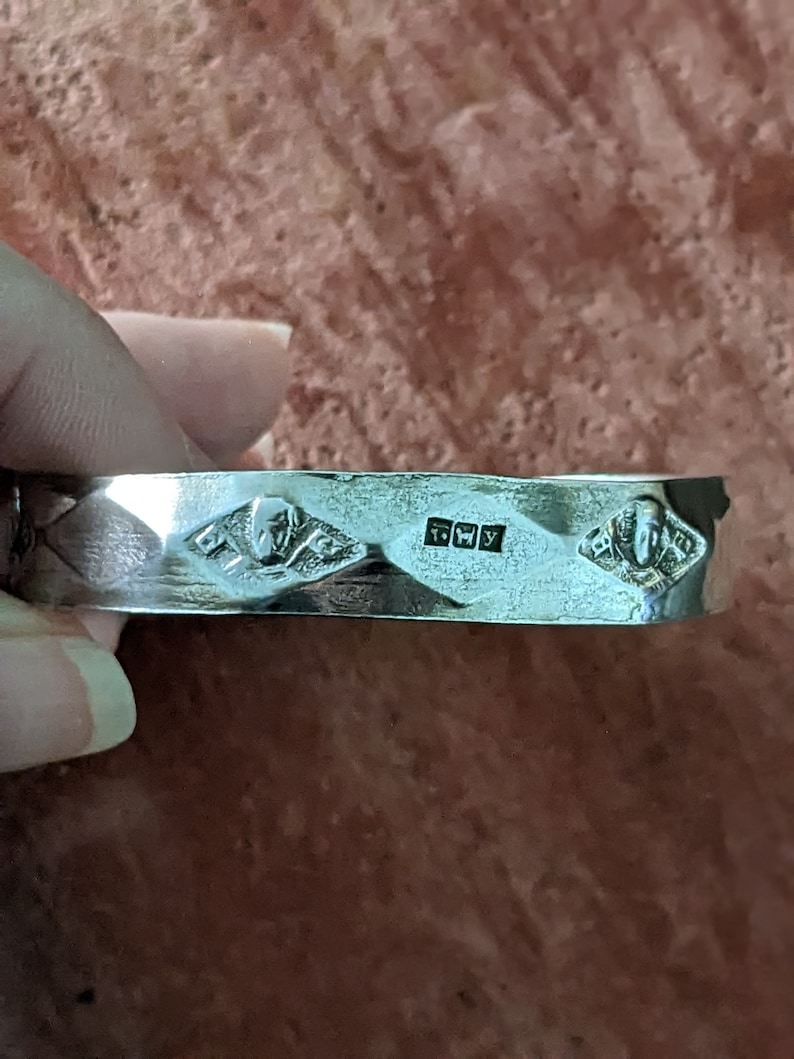May include: A silver bracelet with a textured design and three diamond-shaped markings. The markings include the letters "925" and "FWY".
