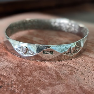 May include: A silver ring with a textured surface and a hallmark on the inside. The ring has a geometric design with three points.