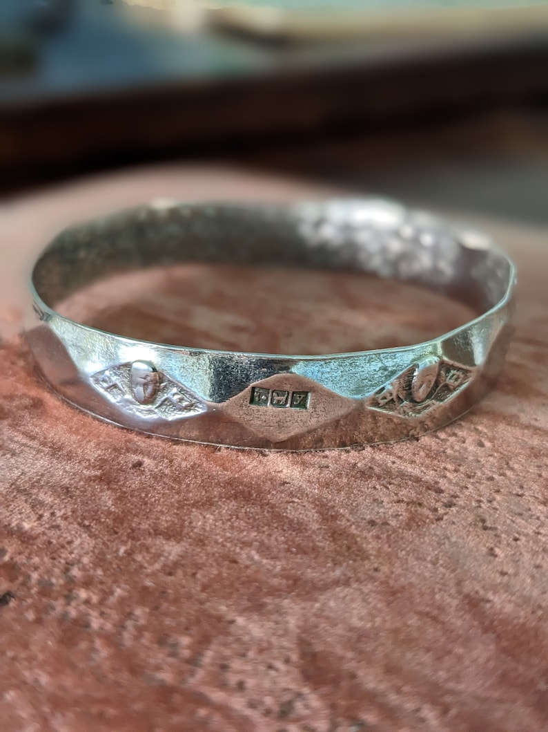 May include: A silver ring with a textured surface and a hallmark on the inside. The ring has a geometric design with three points.