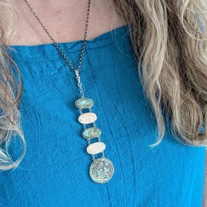 May include: A silver chain necklace with a pendant made of multiple oval and round turquoise-colored stones. The stones are set in silver and have a textured surface.