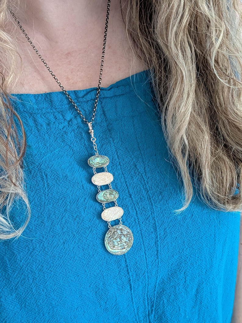 May include: A silver chain necklace with a pendant made of multiple oval and round turquoise-colored stones. The stones are set in silver and have a textured surface.