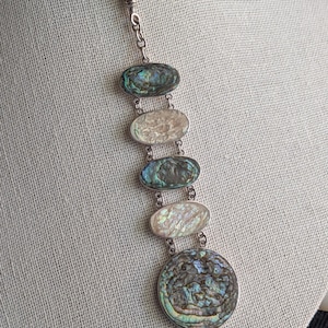 May include: A silver chain necklace with a pendant featuring five oval-shaped abalone shell pieces and a larger round abalone shell piece.