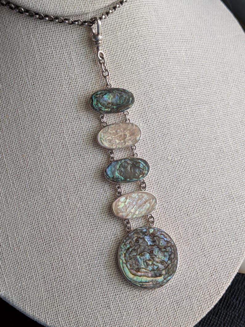 May include: A silver chain necklace with a pendant featuring five oval-shaped abalone shell pieces and a larger round abalone shell piece.