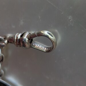 May include: Close-up of a silver pocket watch chain with a clasp that reads "STERLING".