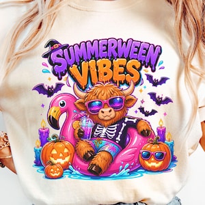 以下が含まれることがあります： クリーム色のTシャツ。カラフルなグラフィックが特徴で、サングラスをかけたハイランド牛がピンクのフラミンゴの浮き輪に乗っています。テキスト「Summerween Vibes」が牛の上に表示されています。
