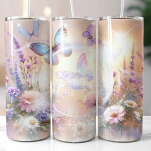 May include: A floral-themed tumbler with a light pink background, featuring butterflies, flowers, and the text "In Loving Memory." The design includes lavender, daisies, and pink flowers, with a sparkling effect. The tumbler has a straw and a silver lid.