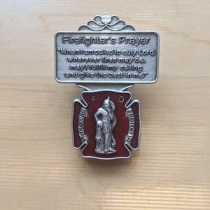 Könnte beinhalten: Ein silberner Feuerwehr-Gebetsanhänger mit einem roten Emaille-Mittelteil, das einen Feuerwehrmann mit einem Wassereimer zeigt. Der Anhänger trägt die Inschriften "Firefighter's Prayer" und "St. Florian Protect Us".
