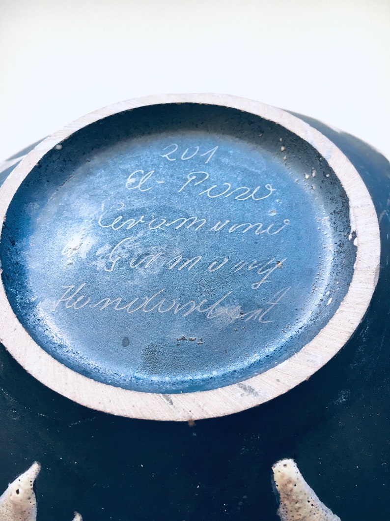 May include: A blue ceramic vase with a white rim and a handwritten inscription on the bottom that reads "201 el Porro ceram uni 6.5 cm my Hundeblatt".