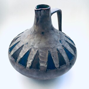 May include: A brown ceramic pitcher with a geometric design of black triangles around the base. The pitcher has a wide mouth and a handle.