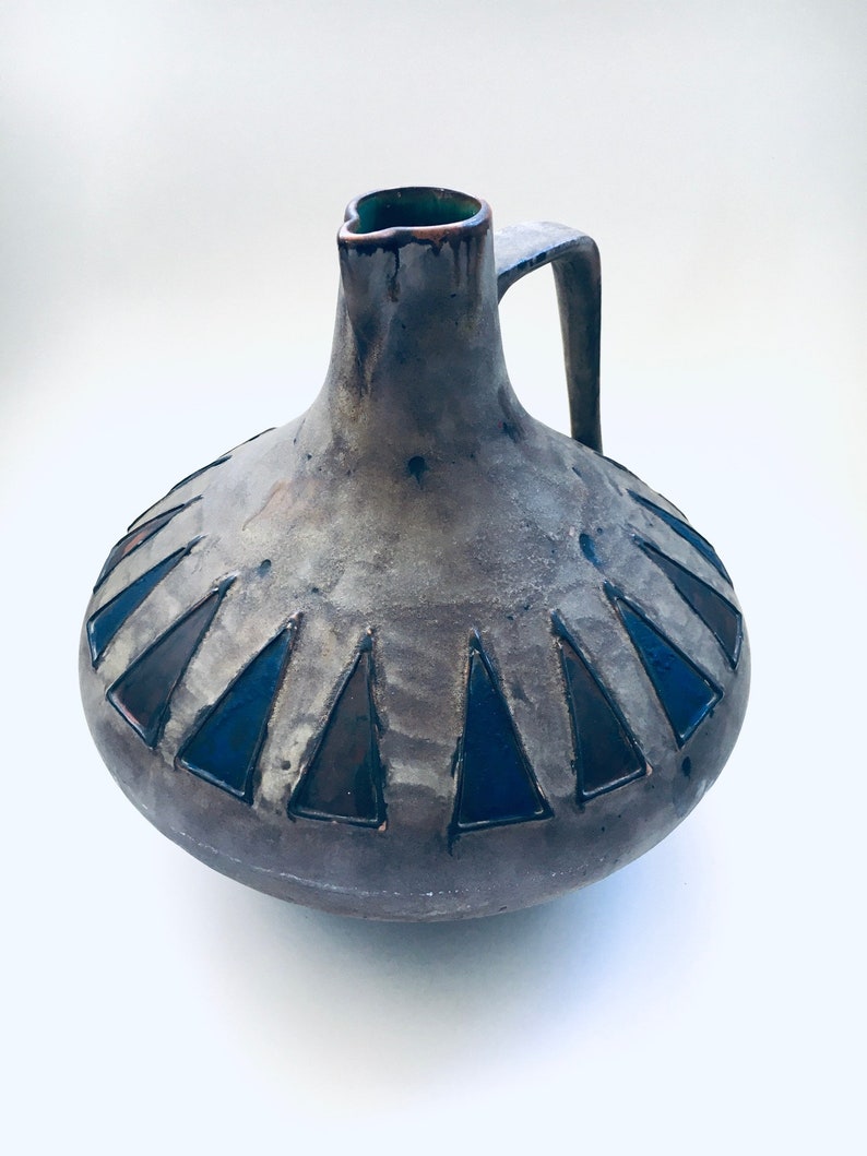 May include: A brown ceramic pitcher with a geometric design of black triangles around the base. The pitcher has a wide mouth and a handle.