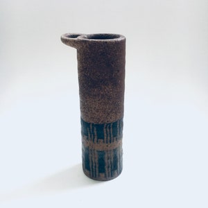 Può includere: Un vaso in ceramica marrone con un motivo geometrico nero e un manico sul lato.