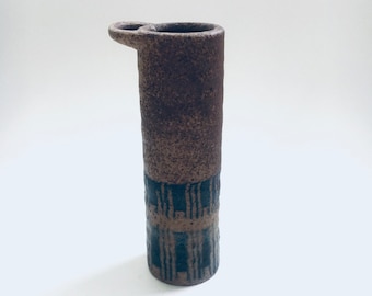 May include: A brown ceramic vase with a black geometric pattern and a handle on the side.
