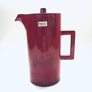 May include: A red ceramic jug with a handle and a lid. The jug has a label that says "kerily stile nuovo".