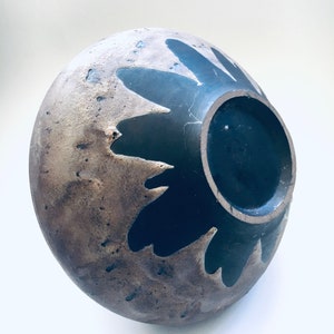 May include: A ceramic bowl with a brown and black glaze. The bowl has a unique design with a black flower pattern.
