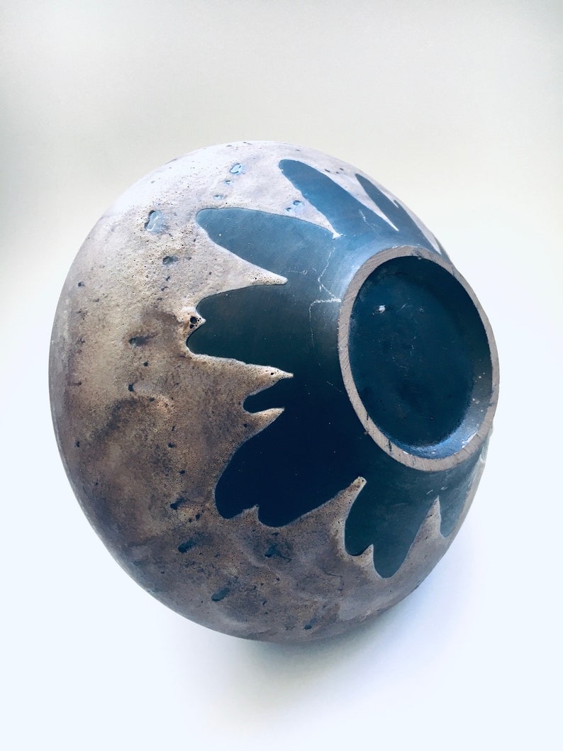 May include: A ceramic bowl with a brown and black glaze. The bowl has a unique design with a black flower pattern.