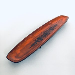 Puede incluir: Un plato de servir de cerámica largo y estrecho de color naranja con un diseño de árboles negros. El plato es ligeramente curvo y tiene un acabado brillante.