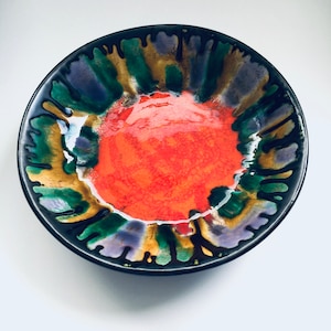 Puede incluir: Un cuenco de cerámica negra con un esmalte colorido. El cuenco tiene un centro rojo con acentos verdes, morados y dorados.