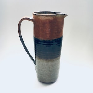 May include: A brown, black, and white ceramic pitcher with a wide mouth and a handle. The pitcher has a rustic, handmade look.