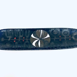Puede incluir: Un plato de servir largo de cerámica negra con un diseño geométrico blanco y gris en el centro. El diseño presenta un círculo con una estrella de cuatro puntas en su interior. El plato está decorado con acentos rojos y negros.