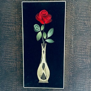 May include: A framed string art piece depicting a red rose in a white vase on a black background.