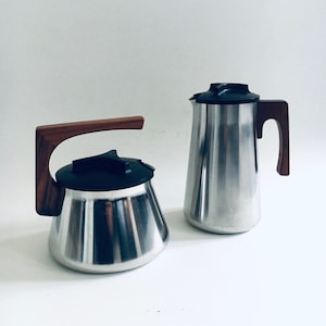 Puede incluir: Un juego de dos cafeteras de acero inoxidable con asas de madera. Las cafeteras tienen tapas negras y un diseño elegante y moderno.