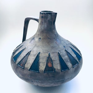 May include: A ceramic pitcher with a brown and gray glaze and a blue and black geometric design. The pitcher has a wide base and a narrow neck.