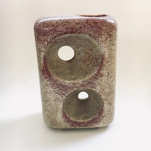 May include: A rectangular ceramic vase with two large circular openings. The vase has a speckled, textured surface with shades of brown and tan, and reddish-brown accents around the openings. The top has a small opening.