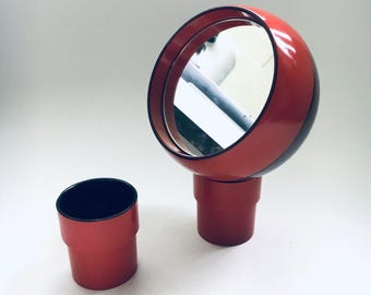 May include: A red and black round mirror with a stand and a matching red and black cylindrical container.