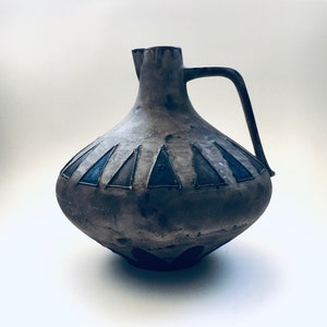May include: A brown ceramic pitcher with a wide base and a handle. The pitcher has a geometric design of triangles in shades of blue and brown.