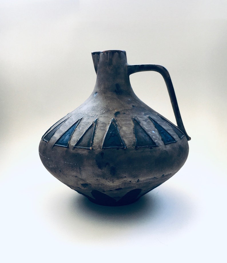 May include: A brown ceramic pitcher with a wide base and a handle. The pitcher has a geometric design of triangles in shades of blue and brown.