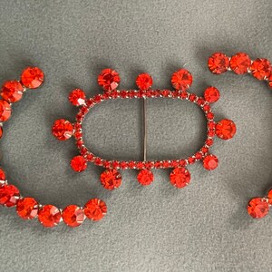 May include: Three red rhinestone jewelry pieces, two are circular and one is a buckle with a center bar.