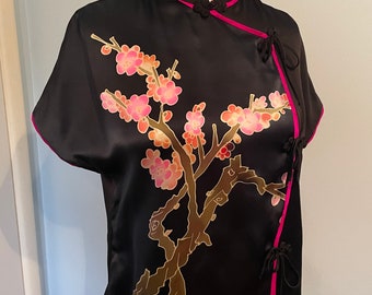 May include: Black silk top with a gold and pink floral design and a pink trim. The top has a mandarin collar and ties at the sides.