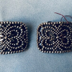 May include: A pair of silver-toned metal square-shaped brooches with a design of black beads and rhinestones. The brooches have a French tag attached to one of them that reads "French 92.306".