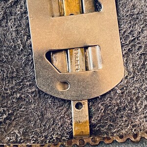 May include: Close-up of a metal buckle with the word "France" engraved on it. The buckle is attached to a brown leather strap.