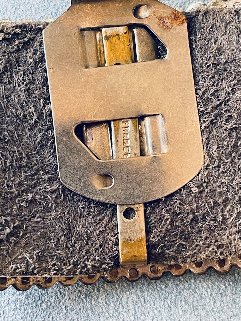 May include: Close-up of a metal buckle with the word "France" engraved on it. The buckle is attached to a brown leather strap.