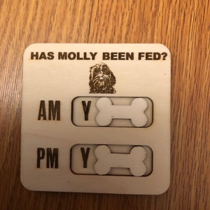 May include: Wooden dog feeding tracker with the text "HAS MOLLY BEEN FED?" and a dog illustration. Features AM and PM sections with bone-shaped sliders to indicate if the dog has been fed.