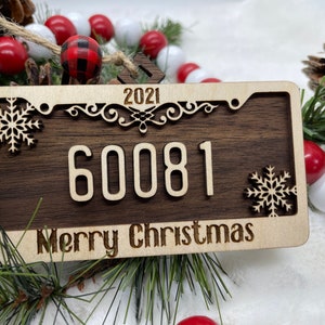 May include: A wooden Christmas ornament shaped like a licence plate with the year 2021, the number 60081, and the text "Merry Christmas". The ornament is decorated with snowflakes.