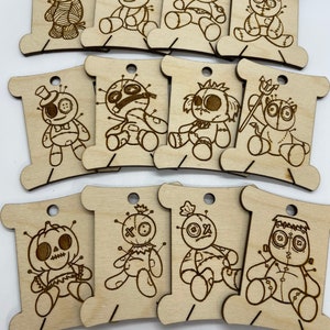 May include: Ten wooden spool thread holders with different voodoo doll designs. Each spool is decorated with a different voodoo doll design, including a pumpkin, a devil, and a traditional voodoo doll.